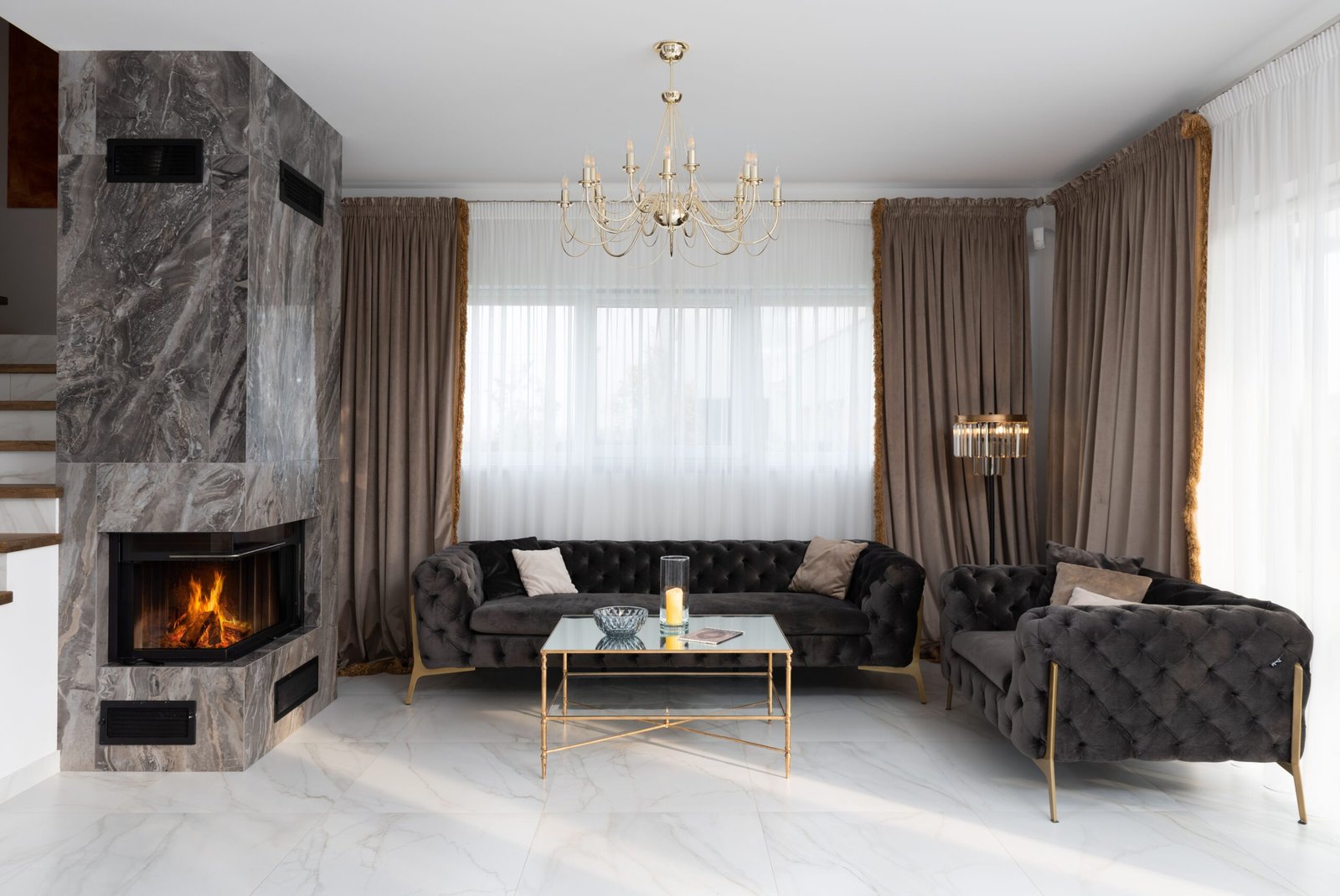 Eleganciki salon w stylu klasycznym z zielonymi sofami chesterfield, kominkiem i kryształowym żyrandolem