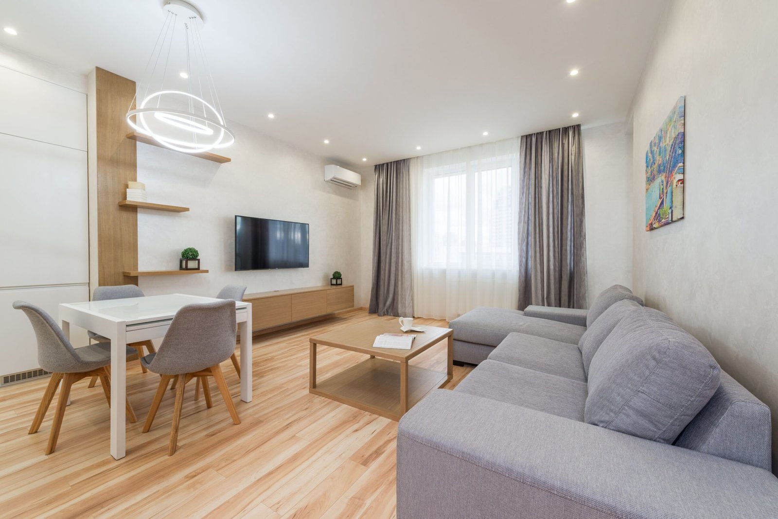 Nowoczesny jasny salon w bloku z szarą sofą na nóżkach, betonową ścianą akcentową i podświetleniem LED