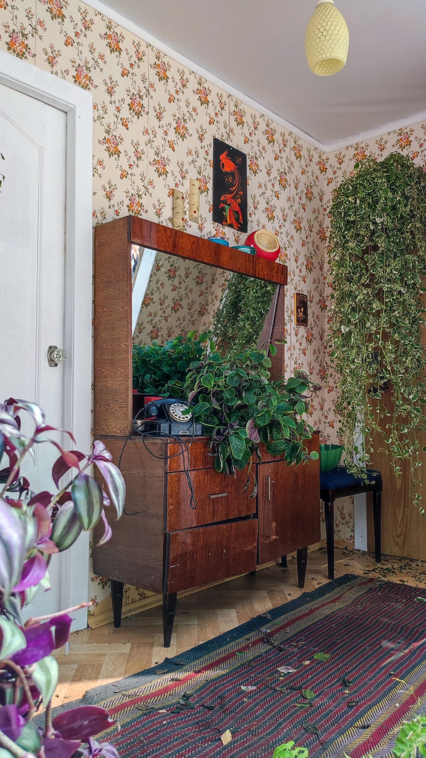 Przedpokój w stylu retro z drewnianą komodą mid-century, okrągłym lustrem i wzorzystą tapetą